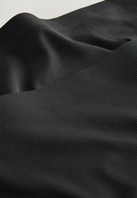 Zwarte stof met een ribbelstructuur, met zachte plooien en een subtiele glans. Het ontwerp is glad met een consistent patroon overal.