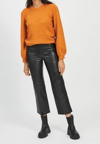 Orange knitted sweater with long sleeves, paired with high-waisted black leather cropped pants and black ankle boots.
