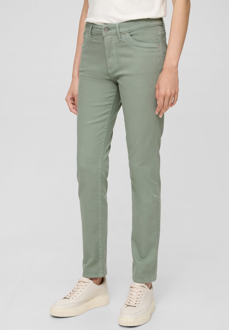 Jasnozielone dżinsy z mieszanki bawełny, o dopasowanym kroju, z przednimi kieszeniami i kontrastowymi szwami, noszone z beżowymi sneakersami.