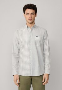 Camisa de botones en un patrón de cuadros en gris claro y blanco, con mangas largas, cuello y un bolsillo en el pecho que presenta una etiqueta de logo.