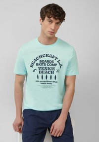 Lichtblauwe katoenen t-shirt met een donkerblauw grafisch ontwerp met tekst en iconen, ronde halslijn en korte mouwen.