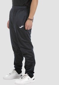 Navy Trackpants aus glattem Stoff, mit einem elastischen Bund und einem weißen Logo am linken Bein. Tragen sie mit weißen Sportschuhen.