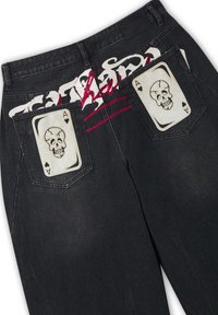 Schwarze Jeans mit weißen Totenkopf-Ass-Spielkartendesigns auf den Gesäßtaschen und stilisierten weißen und roten Schriftzügen über dem oberen Rücken.