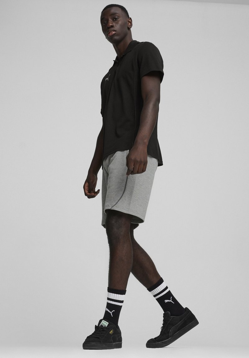 Zwarte poloshirt met korte mouwen, grijze korte broek, zwarte sneakers en gestreepte sokken. De kraag heeft een zichtbaar logo. Minimalistisch ontwerp.