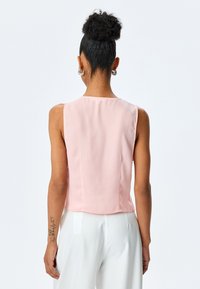 Hellrosa ärmellose Bluse mit glatter Textur, rundem Ausschnitt und geradem Schnitt am Saum, kombiniert mit weißen hoch taillierten Hosen.