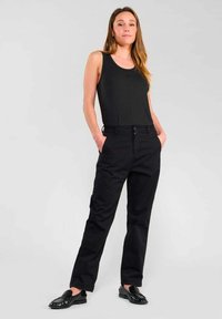 Zwarte tanktop gecombineerd met zwarte, recht gesneden broek. De outfit heeft een gladde textuur en minimale details, aangevuld met zwarte instappers.