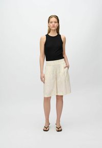 Black ribbed tank top paired with lightweight, cream shorts featuring a subtle floral pattern and an elastic waistband with pockets.