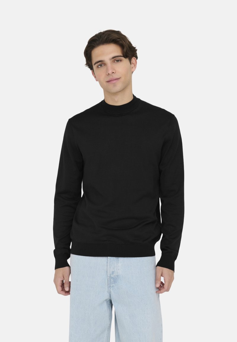 Maglione nero a maniche lunghe con un collo alto, polsini e fondo a coste, realizzato in un tessuto morbido ed elastico. Abbinato a jeans in denim azzurro chiaro.