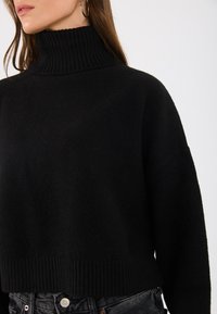 Schwarzer, grob gestrickter Pullover mit einem hohen gerippten Rollkragen und lässiger Passform. Verfügt über eine strukturierte Oberfläche und einen verkürzten Saum.