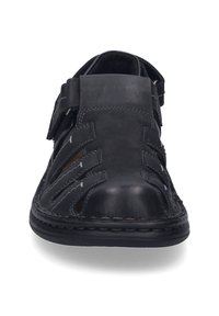 Black leather sandal with open design, featuring slits on the upper, adjustable strap, and stitched detailing around the sole.
