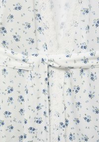 Robe florale composée d'un tissu blanc avec des imprimés bleus et verts, accentuée d'une délicate bordure en dentelle au centre et d'un lien en tissu à la taille.