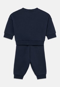 Κοντομάνικο φούτερ από βαμβάκι σε ναυτικό μπλε, συνδυασμένο με αντίστοιχο φαρδύ παντελόνι με στενή εφαρμογή. Διαθέτει ριμπ μανσέτες και στρογγυλή λαιμόκοψη.