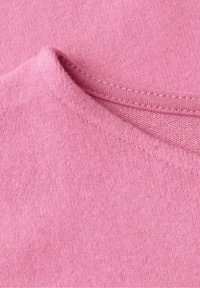 Gros plan d’un tissu tricoté rose montrant un bord plié et un détail de couture sur une surface douce et texturée.