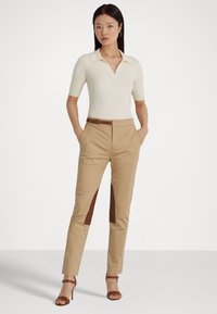 Μπεζ ραμμένα παντελόνια με καφέ πλευρικές λεπτομέρειες, συνδυασμένα με κρεμ πουλοβερ μπλούζα με ρίγες. Οι καφέ ψηλοτάκουνες σανίδες ολοκληρώνουν την εμφάνιση.