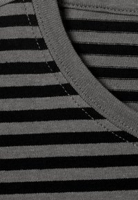Tissu rayé noir et gris avec un col rond à côtes, présentant des détails de couture subtils. Texture douce en gros plan.