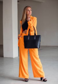 Bright orange suit with wide-leg pants and a cropped black top. Black leather tote bag with short handles. Solid color, smooth texture.