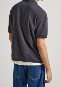 Mörkgrå pikétröja med kort ärm i en texturerad tyg, med en diskret krage och en avslappnad passform, kombinerad med blå denimjeans.