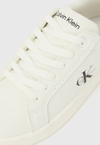 Weißer Sneaker aus glattem, lederähnlichem Material mit weißen Schnürsenkeln, schwarzem "Calvin Klein"-Logo und dezenten Nahtdetails.