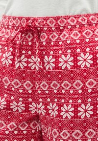 Pantalon de pyjama rouge à motifs, présentant un design floral et géométrique blanc, avec une texture douce et une taille à cordon.