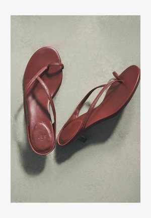 Pár bordových kožených slingback sandálok s otvorenou špičkou, tenkými remienkami, plochou podrážkou a nízkym podpätkom na svetlosivej ploche.
