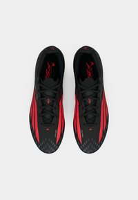 Μαύρα και κόκκινα αθλητικά παπούτσια με αεροδυναμικό σχεδιασμό, που διαθέτουν υφή στο επάνω μέρος και έντονα σχέδια στη σόλα για καλύτερη πρόσφυση.