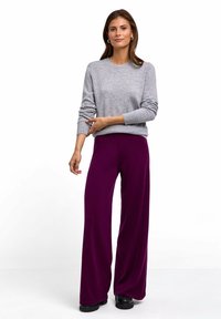 Grauer Strickpullover mit langen Ärmeln, kombiniert mit weiten lila Hosen. Das Outfit zeichnet sich durch eine lockere Passform und eine glatte Textur aus.