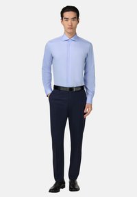 Světle modrá košile na knoflíky s dlouhými rukávy, spárovaná s tmavě modrými kalhotami a černým koženým páskem. Černé boty doplňují celý outfit.