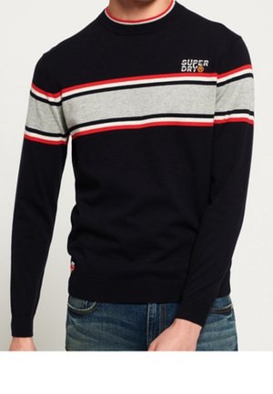 Navy sweater with gray, red, and white horizontal stripes across chest and sleeves, worn with blue jeans.