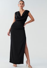 Zwarte avondjurk met een gedrapeerde halslijn, korte mouwtjes en een hoge split aan de dij. Glad, rekbaar materiaal zorgt voor een getailleerd silhouet.