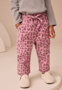 Ružové nohavice s leopardím vzorom, elastickým pásom a šnúrkou, s bočnými vreckami a voľným strihom, v kombinácii s nadýchanými bielymi papučami.