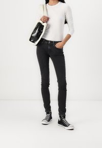 Jeans negros ajustados, camisa blanca de manga larga y zapatillas negras de caña alta. El bolso tiene una superficie negra brillante y asas blancas esponjosas.