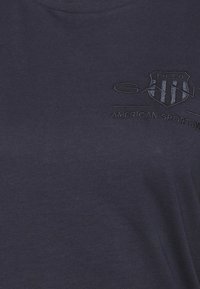 Camiseta de algodón azul marino con cuello redondo, que presenta un logo en relieve y el texto "AMERICAN SPORTSWEAR" bordado en un tono más claro debajo del emblema.