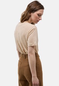 Haut en tricot beige à manches courtes avec une coupe décontractée, associé à un pantalon marron taille haute doté de poches arrière et d'une finition texturée.