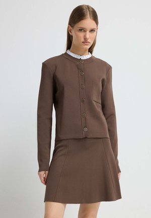 Bruine tweedelige outfit met een cropped button-up jas met een zak en een uitlopende rok. Gemaakt van een gladde, gestructureerde stof.