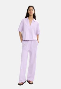 Liliowy, dwuczęściowy strój składający się z krótkiego rękawa, koszuli z kołnierzykiem oraz szerokich spodni, obie części o miękkiej fakturze i z przednimi kieszeniami.