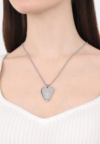 Collar de pendant de plata con forma de pua de guitarra, que presenta un logo y un diseño grabados, colgando de una delicada cadena de bolas.