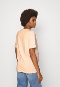T-shirt de manga curta na cor bege clara, feito de material suave com um corte descontraído, apresentando um decote redondo e costuras visíveis.