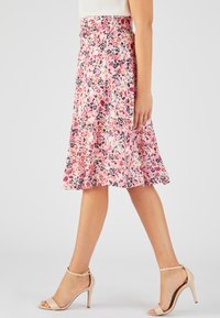 Falda midi floral en rosa y blanco con detalles en negro. Diseño fluidos con estampados vibrantes de hojas. Combinada con sandalias de tacón nude.