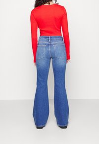 Camiseta de manga larga roja con textura de canalé, combinada con unos vaqueros acampanados de tiro alto en azul, que cuentan con un diseño clásico de cinco bolsillos y detalles de costura visibles.