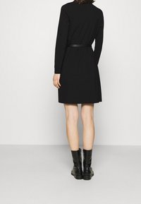 Robe noire à manches longues avec une taille cintrée et une jupe droite, associée à des bottines noires à design texturé.