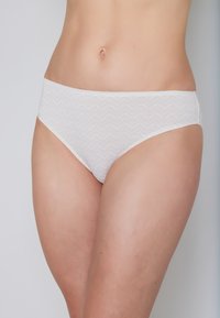 White women's bikini-style underwear with a zigzag pattern, featuring a smooth texture and mid-rise design. No visible hardware or accents.