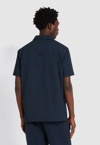 Camicia navy a maniche corte con colletto e dettaglio anteriore, realizzata in tessuto leggero, caratterizzata da una texture liscia e una vestibilità rilassata.