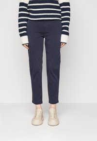 Marinblå bomullbyxor med slim fit och uppvikt nederkant, ihop med beige sneakers med en strukturerad ovandel och snörning. Randig tröja synlig.