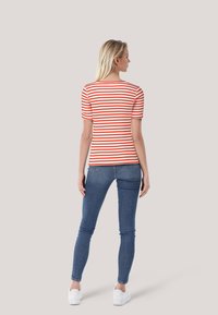 Rot-weiß gestreiftes T-Shirt mit kurzen Ärmeln, kombiniert mit blauen Skinny-Jeans und weißen Sneakers; glatter Stoff und taillierte Passform.