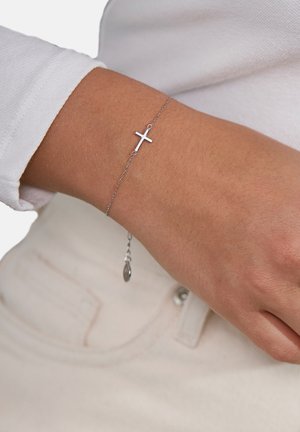 Sølvarmbånd med en lille korsvedhæng, en fin kæde og justerbar længde med en dråbeaccent. Glat metaloverflade.