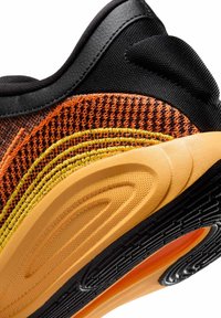 Sportsko med en flerfarvet mesh-overdel i orange, gul og sort, med en tekstureret gummisål og glatte sorte detaljer.