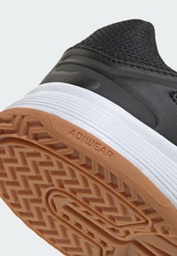 Čierna športová obuv s textúrovaným zvrškom, bielou medzipodrážkou a gumovou podrážkou s cik-cak vzorom a značkou "ADIWEAR".