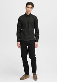 Black long-sleeve button-up shirt with a classic collar, smooth texture, front buttons, paired with black jeans and light brown shoes.