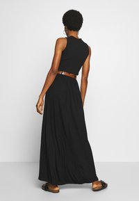 Top negro sin mangas combinado con una falda maxi negra fluida, con un cinturón marrón y sandalias planas, mostrando una textura suave.