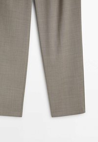 Pantalon de costume droit marron clair avec un motif textile subtilement texturé, visible de la cuisse jusqu’à l’ourlet.